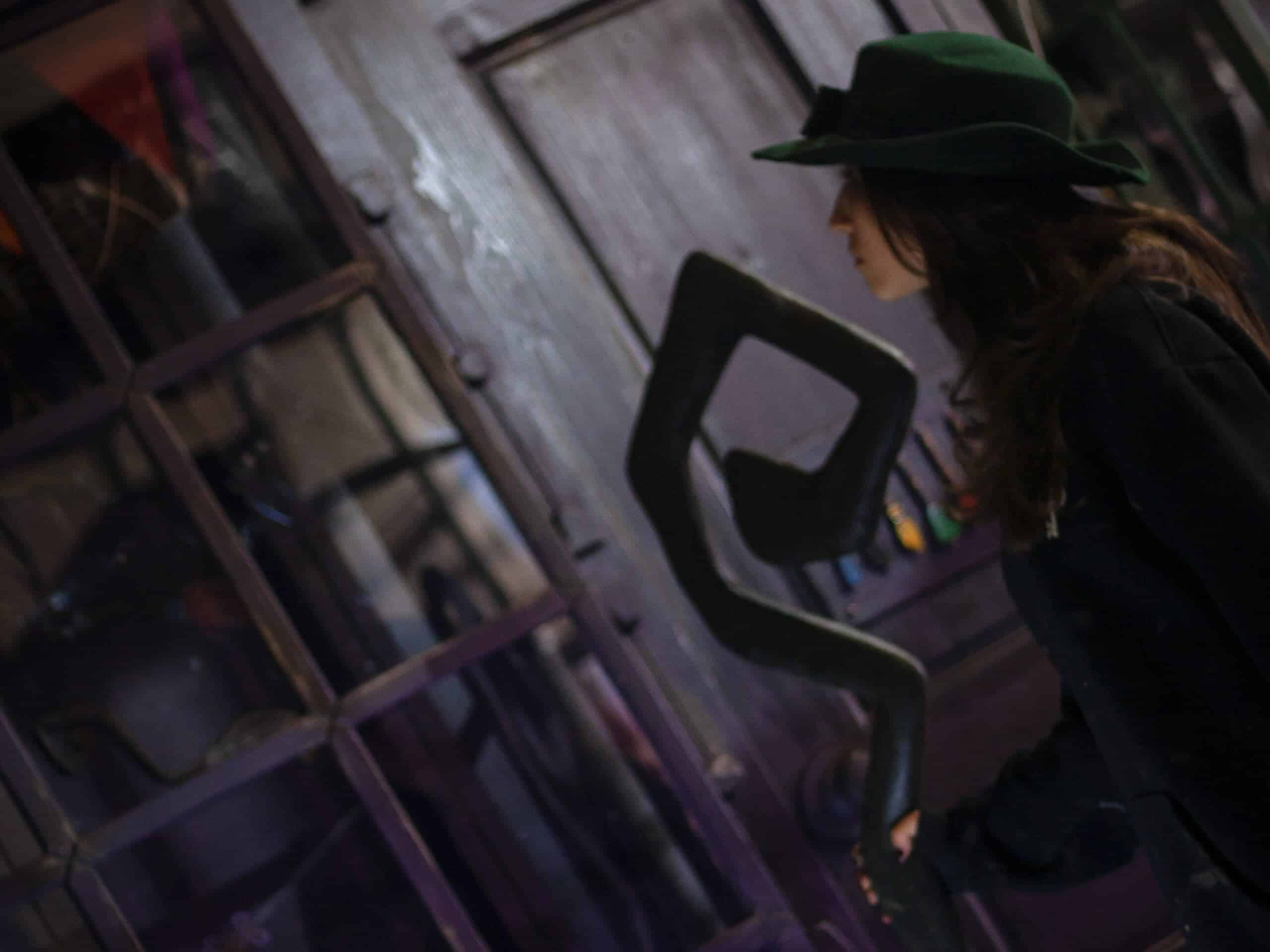 Vintage escape room with a woman in a black hat exploring puzzles inside a rustic setting.